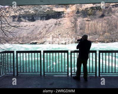 Un photographe prend des photos le long de la rivière Niagara, juste en dessous des chutes Niagara, sur le White Water Walk, une attraction populaire des parcs du Niagara. Banque D'Images