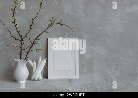 Cadre photo vierge à côté des branches de prune de cerise dans une cruche et des bougies sur une cheminée Banque D'Images