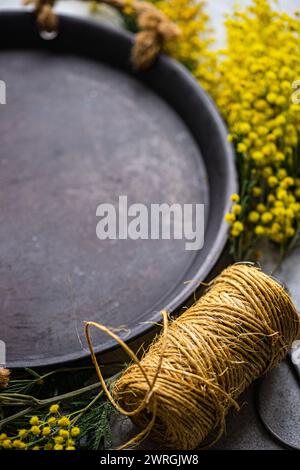 Gros plan plein cadre de fleurs de mimosa jaune et de ficelle à côté d'un plateau en métal rustique sur une table Banque D'Images