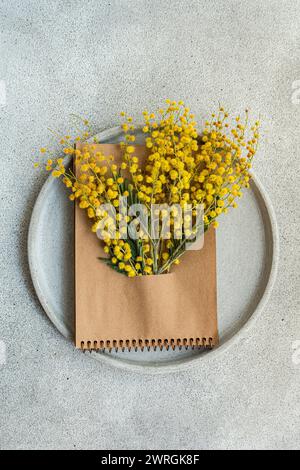 Vue aérienne d'un bouquet de fleurs de mimosa jaunes nichées dans un bloc-notes sur une assiette Banque D'Images