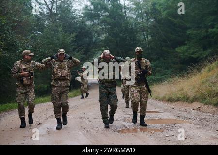 Un groupe de soldats d'élite conduit les captifs dans un camp militaire, mettant en évidence une atmosphère tendue de détention et d'opérations de sécurité Banque D'Images