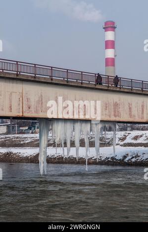 De gros morceaux de glaçons pendent de la partie inférieure du pont métallique sur le fleuve Vardar à Skopje. Banque D'Images