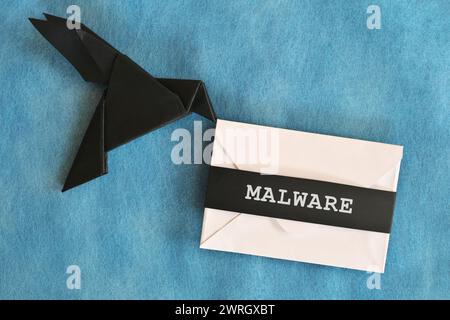 Noir corbeau papier origami portant une enveloppe de lettre blanche avec mot malware. Concept de réception d'e-mails d'attaque de logiciels malveillants. Banque D'Images