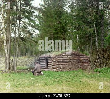 Cabane dans la forêt, pour bûcherons et kuria (combustion de charbon), 1912. Petite cabane en rondins à côté des bois avec l'homme assis sur le rondin à proximité. Banque D'Images