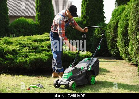 Jeune homme fixant la tondeuse à gazon dans le jardin Banque D'Images