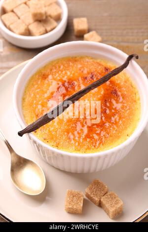 Délicieuse crème brûlée dans un bol, gousse de vanille, cuillère et cubes de sucre sur la table, gros plan Banque D'Images
