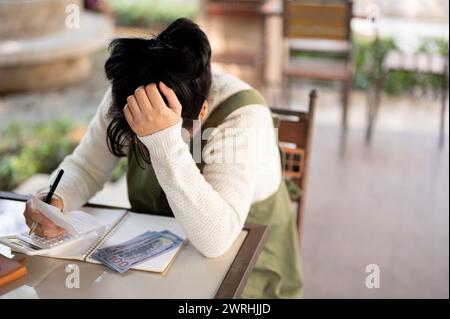 Une jeune femme asiatique déçue et stressée propriétaire de petite entreprise connaît une crise financière et la faillite, inquiète pour sa boutique mensuelle Banque D'Images
