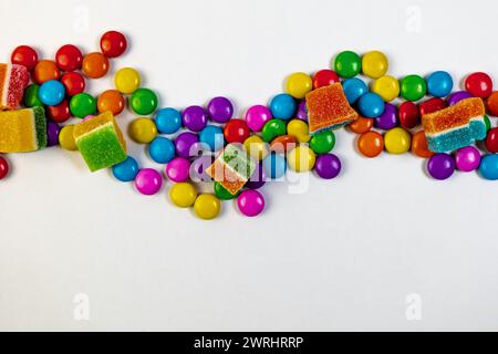 Un éclat de bonbons colorés de différentes formes et tailles, dispersés sur un fond blanc propre. Vue de dessus Banque D'Images