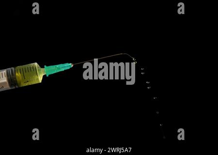 Seringue avec aiguille, une rangée de gouttes de liquide jaune sortant, isolé sur fond noir et espace de copie Banque D'Images