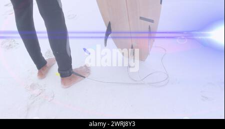 Image de faisceaux lumineux se déplaçant sur les pieds du surfeur sur la plage tenant la planche de surf Banque D'Images