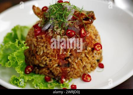 Cuisine thaïlandaise, riz au jasmin frit avec maquereau de poisson en conserve dans une sauce tomate, garni de piment rouge, d'oignon rouge, de laitue et de feuilles de citron vert kaffir. Banque D'Images