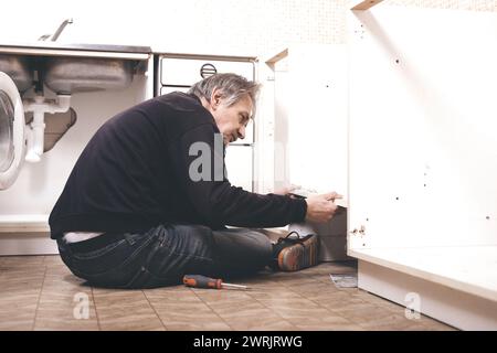 Homme plus âgé démontant la cuisine de l'appartement hors service Banque D'Images