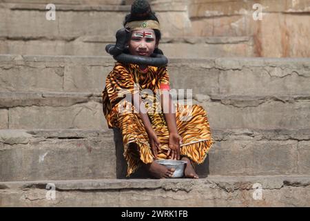 Varanasi, Inde- 13 mars 2019 : une petite fille est habillée d'un costume de tigre, a un faux serpent autour du cou et supplie pour de l'argent à Varansi Banque D'Images