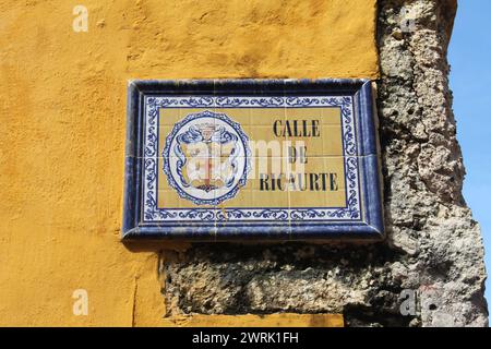 Cartagena, Columbia- 1er décembre 2016 : un panneau de tuile sur un mur peint en jaune, aperçu de briques et le ciel note le nom de rue de Calle de Ricaurte Banque D'Images