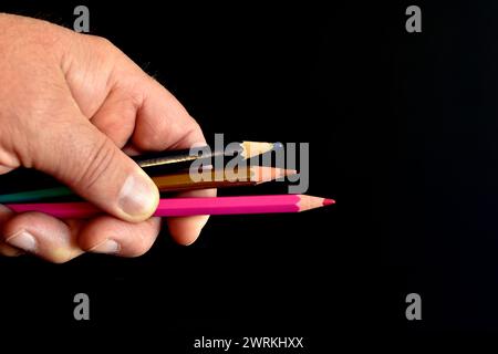 La main d'un homme dans laquelle il tient trois crayons de couleur. Banque D'Images