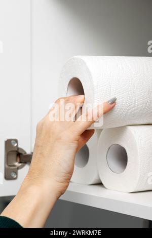 la femme au foyer sort un rouleau de papier essuie-tout de l'armoire de cuisine. essuie-tout dans le placard. photo verticale Banque D'Images