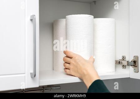 la femme au foyer sort un rouleau de papier essuie-tout de l'armoire de cuisine. essuie-tout dans le placard. à l'aide d'une serviette en papier Banque D'Images