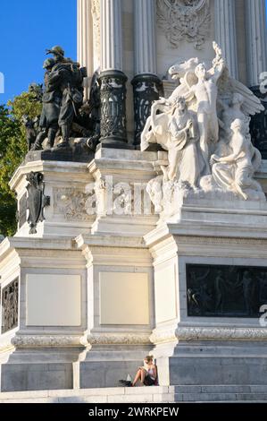 Jeune femme se relaxant lisant un livre au pied du monument du roi Alphonse XII dans le parc Buen Retiro (Parque del Buen Retiro), Madrid, Espagne, Europe Banque D'Images