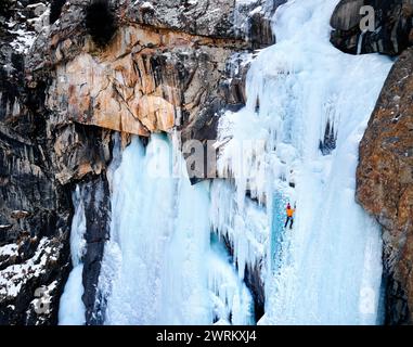 Vue aérienne drone de l'athlète en veste orange escalade de glace à grande cascade gelée dans la gorge Barskoon la vallée de montagne au Kirghizistan Banque D'Images