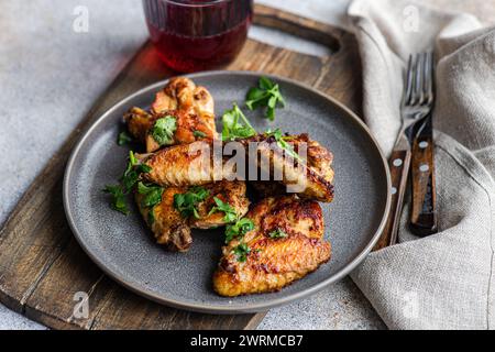 Succulentes ailes de poulet rôties glacées dans une sauce épicée, garnies de feuilles de coriandre fraîches, accompagnées d’un cocktail de cerises, le tout servi sur un plan rustique Banque D'Images