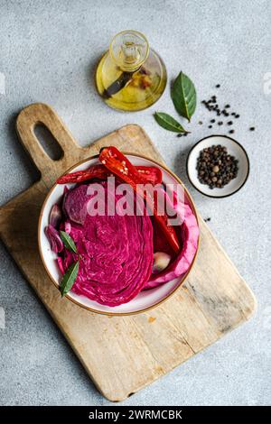 Une vue de haut en bas de chou fermenté avec betterave, garni de poivron rouge épicé, d'ail et de feuilles de laurier, servi dans un bol sur une planche de bois. Banque D'Images