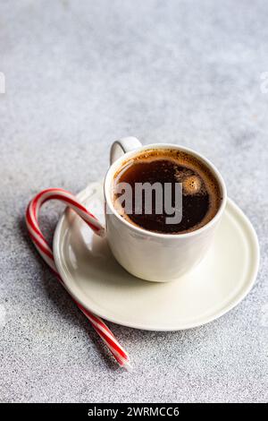 Une scène matinale confortable avec une tasse blanche de café chaud associée à une canne de bonbons rouge et blanc sur une surface grise mouchetée. Banque D'Images
