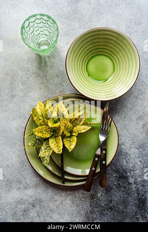 Vue de dessus d'une table sophistiquée composée de plats en céramique vert vif, agrémentés d'élégants couverts et d'un verre décoratif sur un su texturé Banque D'Images