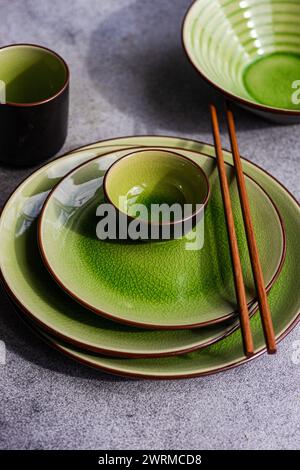 Vue d'en haut d'une table élégante agrémentée d'assiettes et de bols en céramique vert vif, agrémentés de baguettes en bois, le tout disposé sur un textu Banque D'Images