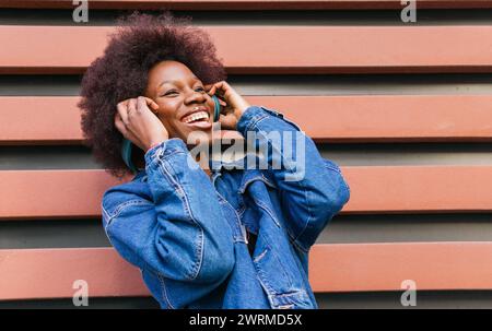 Une jeune femme exubérante au sourire radieux profite de la mélodie dans son casque, créant un moment de bonheur urbain Banque D'Images