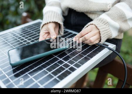 Gros plan des mains d'une personne chargeant un smartphone à l'aide d'un panneau solaire portable. Banque D'Images