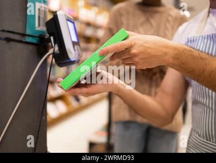 Les mains d'une personne anonyme recadrée sont montrées payer avec une carte à un lecteur de carte pendant le processus de paiement dans une épicerie Banque D'Images