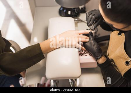 Un client se fait faire les ongles par un manucure portant des gants noirs dans un salon de beauté Banque D'Images