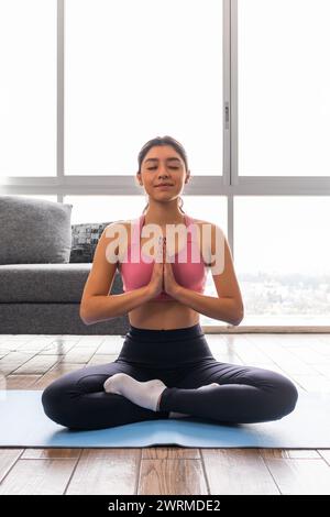 Une jeune femme adulte avec les yeux doucement fermés et les mains pressées ensemble dans Anjali Mudra, rayonne de tranquillité tout en exécutant Padmasana (Lotus Pos Banque D'Images