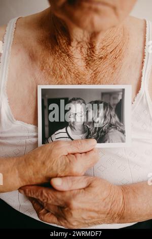 Les mains d'une femme âgée bercent une photographie capturant un tendre baiser sur la joue, évoquant des souvenirs et des émotions Banque D'Images