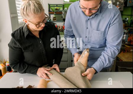 Deux artisans examinent une forme de chaussure au cours du processus méticuleux de fabrication de chaussures à la main dans un atelier de cordonnier lumineux et organisé en Autriche. Banque D'Images