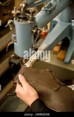 Gros plan des mains d'un cordonnier recadré méconnaissable cousant une chaussure en cuir avec une machine à coudre dans un atelier autrichien, mettant en valeur la tradition Banque D'Images