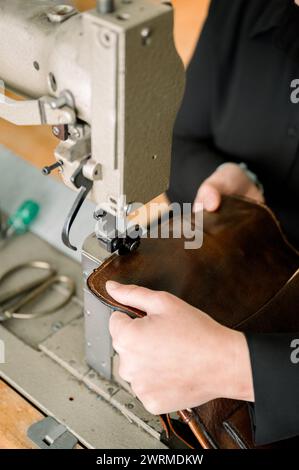 Gros plan des mains d'un cordonnier anonyme fabriquant une chaussure en cuir à l'aide d'une machine à coudre dans un atelier autrichien. Banque D'Images