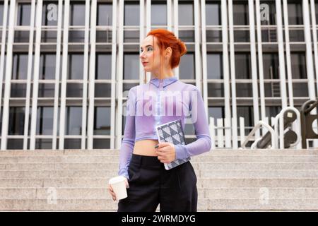 Femme d'affaires moderne dans une blouse transparente violette avec un pantalon noir avec des cheveux roux vifs complétant sa tenue d'affaires audacieuse et non conventionnelle tout en h. Banque D'Images