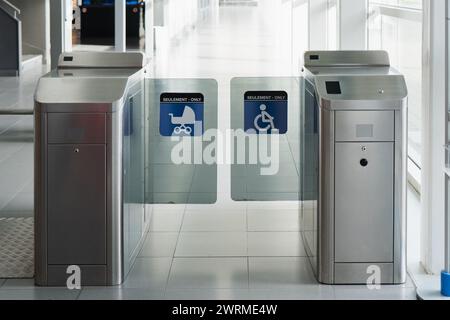 Une image montrant des tourniquets d'entrée modernes avec des lecteurs de billets à l'entrée d'un bâtiment, indiquant les options d'accessibilité pour les personnes handicapées Banque D'Images