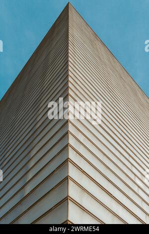 De dessous le coin tranchant du gratte-ciel contre un ciel bleu clair, mettant en valeur un design architectural moderne et des motifs de lignes répétitifs. Banque D'Images