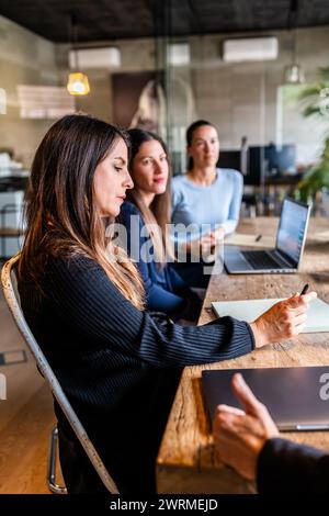 Trois femmes professionnelles ont participé activement à une réunion d'affaires, examinant le contenu sur un ordinateur portable. Banque D'Images