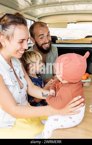 Une famille heureuse partage un moment joyeux ensemble dans un van vintage, rayonnant une atmosphère insouciante et aimante. Banque D'Images