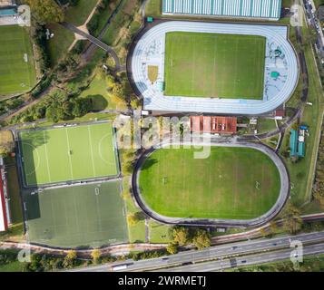 Une photographie de drone descendant montrant divers terrains de sport, y compris une piste de course, un terrain de football et des courts de tennis entourés de verdure et de c Banque D'Images