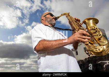 From Below Man joue du saxophone passionnément à l'extérieur, avec un ciel nuageux dramatique comme toile de fond, célébrant l'esprit de la Journée internationale du Jazz Banque D'Images