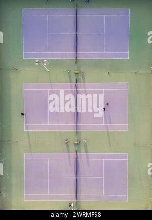 Vue plongeante sur deux courts de tennis avec joueurs engagés dans des jeux, montrant l'agencement du court et l'activité. Banque D'Images