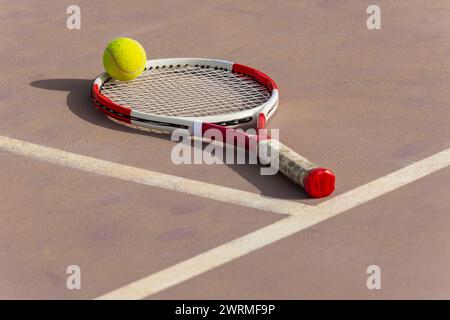 Gros plan d'une raquette de tennis et d'une balle jaune sur un court de terre battue, mettant en évidence les détails de l'équipement du sport. Banque D'Images