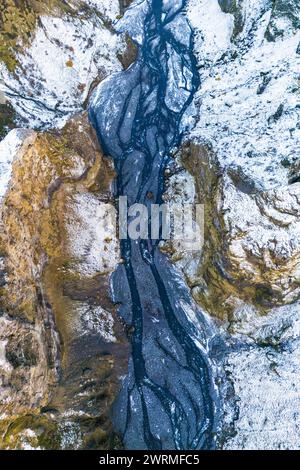 Une prise de vue aérienne capture le chemin complexe d'une rivière du nord serpentant à travers un terrain enneigé en hiver, alliant beauté naturelle et soupçon de mer Banque D'Images