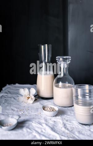 Deux bouteilles en verre de lait d'avoine fait maison avec un verre à moitié plein et l'avoine dispersée sur un chiffon Banque D'Images