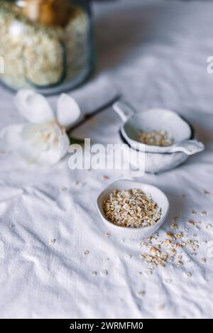 Une installation sereine avec flocons d'avoine faits maison dans un bol en céramique blanche sur un fond texturé clair, accompagné d'un pot en verre et d'un soupçon de fl Banque D'Images