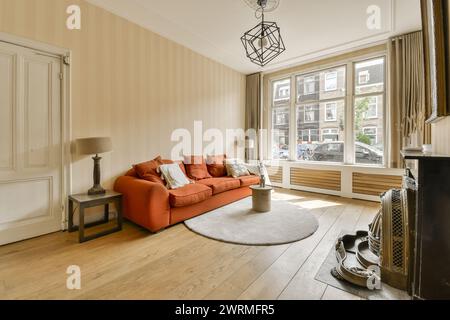 Cette image met en valeur un salon spacieux avec un grand canapé orange, du parquet et des décorations contemporaines, éclairées par la lumière naturelle. Banque D'Images